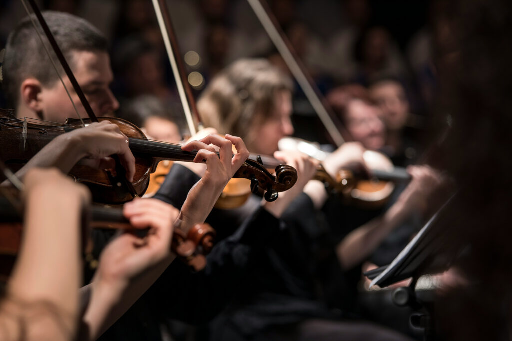 Violinistas de uma orquestra tocando em sincronia, metáfora visual para densidade de talentos em equipes de alta performance